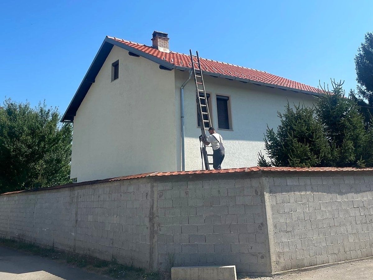 Punëtor në shkallë gjatë pastrimit të fasadës – shtëpi me çati terrakote